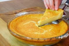 a person cutting into a pie in a glass dish on top of a wooden table