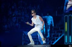 a man in white pants and sunglasses on stage with his hands out to the side