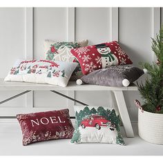 christmas pillows are sitting on a bench next to a potted plant and a pillow