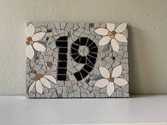 a small mosaic with the letter d on it's side and flowers in the middle