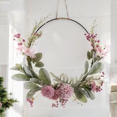 a wreath with pink flowers hanging from the ceiling next to a potted plant in front of a window