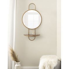 a round mirror hanging on the wall above a bench in a room with white walls