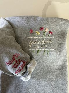 a gray sweater with embroidered flowers and the words grandma estrave written on it's sleeves