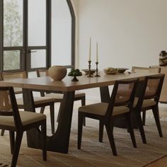 a dining room table with chairs and a vase on top of it in front of a large window