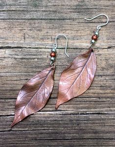 two leaf shaped earrings with beads hanging from them on a wooden surface and wood planks