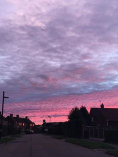 the sky is pink and purple as it sets on an empty street with houses in the background