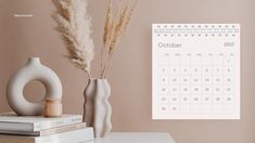 a calendar is on the wall next to some books and a vase with dry grass in it