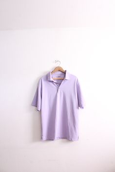 "Pastel lilac colored polo shirt with buttons at the top and loose fit. Ideal 90s basic in good condition. 'Grand Master Golf' brand 100% Polyester Size L Measures: 30\" length 23\" across chest 10\" sleeve 3.5\" tall collar B-3" Casual Purple Cotton Polo Shirt, Purple Collared Cotton Top, Classic Purple Short Sleeve Polo Shirt, Purple Cotton Collared Top, Casual Purple Short Sleeve Polo Shirt, Casual Purple Polo Collar Shirt, Purple Casual Polo Collar Shirt, Casual Purple Polo Shirt, Purple Relaxed Fit Collared Top