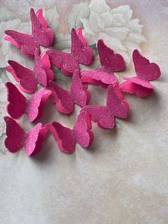 pink paper hearts are arranged on a white surface with flowers in the backgroud