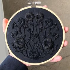 a person holding up a black embroidery on a wooden hoop with flowers in the middle