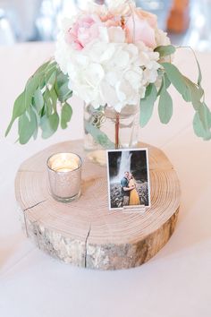 a vase filled with white flowers and greenery next to a candle on top of a table