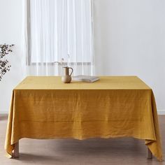 a table with a book and vase on it in front of a white curtained window