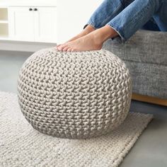 a woman sitting on top of a white ottoman in a living room next to a rug