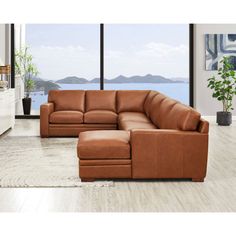 a brown leather sectional sofa sitting on top of a wooden floor next to a large window