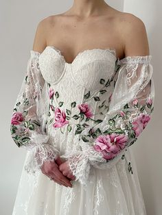 a woman in a white dress with pink flowers on her arm and sleeves, standing against a wall