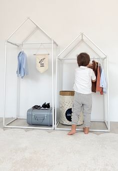 a little boy that is standing in front of a house shaped shelf with clothes on it