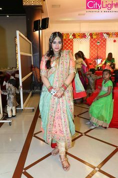 a woman in a green and pink outfit standing on a tile floor with other people