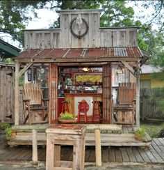 an outdoor bar with chairs and tables on a wooden deck in front of a shed