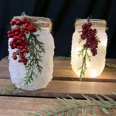 two mason jars decorated with red berries and greenery are sitting on a wooden table