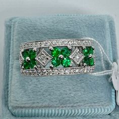 an emerald and diamond ring in a blue velvet box with a white ribbon around it