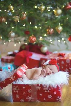 a baby is sleeping in a christmas present box under a tree with presents on the floor