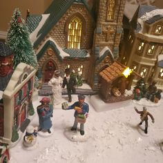 a group of figurines that are standing in the snow with buildings and trees