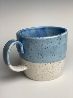 a blue and white coffee cup with speckles on it's side, sitting in front of a gray background