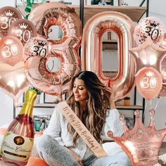 a woman sitting on the floor holding a champagne bottle and balloons in front of her