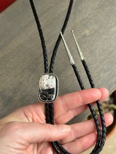 A leather braided cord in black with a cushion cut White Buffalo set in sterling silver. The bolo cord length is 22 inches when held taught, folded. It has sterling silver tips. The "pendant" moves easily enough along the cord but is also snug enough not to move unless given a tug. Tips are not glued on, but rather pinch the cord so it is not recommended to pull the tips while adjusting the "pendant." The setting measures 1-1/4 inches long. Suitable for men and women. Artisan Lariat Jewelry With Adjustable Cord, Handmade Sterling Silver Bolo Tie As Gift, Black Adjustable Bolo Tie For Formal Occasions, Black Western Jewelry With Adjustable Length, Adjustable Silver Artisan Lariat Necklace, Artisan Silver Jewelry With Adjustable Length, Formal Lariat Jewelry With Adjustable Cord, Black Western Style Formal Jewelry, Adjustable Sterling Silver Bolo Tie For Gifts