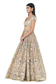 Beige-golden net lehenga with attached cancan, and floral pattern mirror embroidery. Comes with embroidered padded blouse and dupatta.
Components: 3
Pattern: Embroidered
Type Of Work: Mirror
Neckline: Leaf
Sleeve Type: Cap
Fabric: Net
Color: Beige
Other Details: 
Back cutout tassel tie-up blouse
Scalloped hem blouse
Fringed hem lehenga
Occasion: Wedding,Bride - Aza Fashions Elegant Lehenga With Gold Embroidery For Navratri, Elegant Gold Embroidered Lehenga For Navratri, Gold Bollywood Designer Lehenga, Bollywood Style Designer Gold Lehenga, Gold Lehenga Saree With Mirror Work, Gold Embroidered Lehenga For Reception, Gold Lehenga With Mirror Work For Reception, Gold Lehenga With Gold Embroidery For Reception, Gold Embroidered Lehenga For Diwali