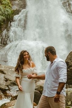 a man and woman standing in front of a waterfall