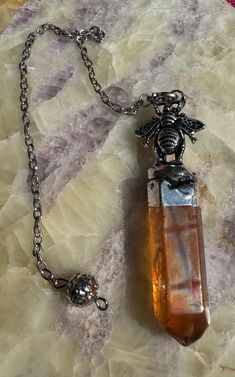 a necklace with an orange stone and a silver chain on top of a marble surface