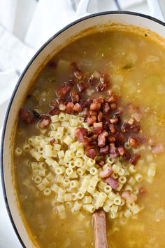 a pot filled with pasta and bacon soup on top of a stove burner next to a wooden spoon