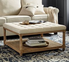 a coffee table with books on it in front of a couch and rug, next to a window