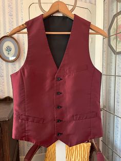 This handsome vest is burgundy with a black sheen/shift on one side and solid black on the other side! It has the original buttons, with three outer pockets on the burgundy side (two of them haven't been opened/unstitched yet) and one chest pocket on the black side. The measurements, taken with the vest lying flat, are: shoulder to shoulder, 12 inches; armpit to armpit, 19 inches; length, 25 1/2 inches in front and 22 inches in back; bottom edge, 17 1/2 inches. In very good condition. Burgundy Vest Outfit Men, Maroon Vest Outfit Men, Fitted Winter Vest With Pockets, Winter Fitted Vest With Pockets, Fitted Solid Vest For Winter, Red Fitted Sleeveless Outerwear, Fitted Red Sleeveless Outerwear, Fitted Red Winter Vest, Fitted Red Vest For Winter