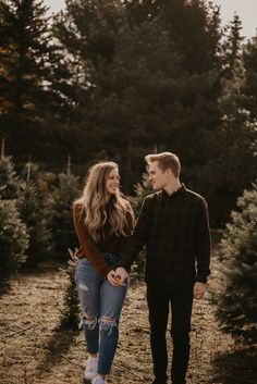 a couple holding hands and walking through the trees at their christmas tree farm engagement session