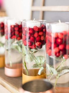 candles are lined up in glass vases with red berries and greenery on them