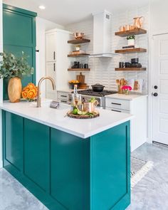 a kitchen with green cabinets and white marble counter tops, an island in the middle