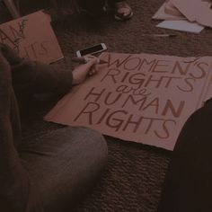 two people sitting on the floor with protest signs and cell phones in front of them