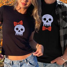 Get ready to celebrate Halloween in style with our matching couple's skull t-shirts! Featuring a spooky skull and bow graphic on a trendy 90's style fit BABYTEE for women, and a skull and BOW-TIE graphic on a unisex cotton t-shirt for men, sold separately. MIX AND MATCH these awesome shirts with your FRIEND GROUP! Perfect for COUPLES, friends, husbands & wives, brides and grooms...looking to show off their spooky spirit together. These  t-shirts are made for comfort and style, ensuring you stand Playful Pre-shrunk Tops For Halloween, Halloween Graphic Print Top As Gift, Halloween Themed Cotton Tops, Playful Crew Neck Tops For Halloween, Cotton Halloween Themed Tops, Themed Cotton Tops For Halloween, Spooky Fitted Halloween Tops, Spooky Fitted Tops For Halloween, Cute Fall Party Tops