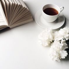 an open book, coffee cup and flowers on a white table