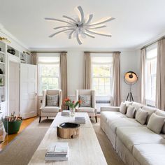 a living room filled with lots of furniture next to a window covered in white curtains