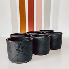 four black cups sitting next to each other on a white table with colorful stripes in the background