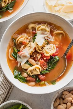 two bowls filled with pasta and spinach soup next to some other dishes on the table