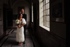 a bride and groom standing together in an old building with sunlight streaming through the windows