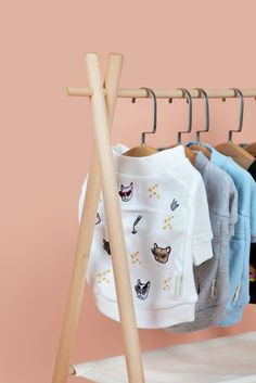 clothes hanging on a rack in front of a pink wall with a wooden hanger