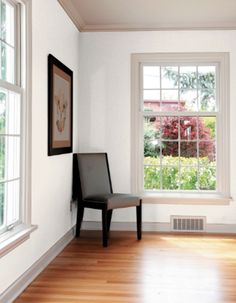 an empty room with two windows and a chair next to it on a hard wood floor