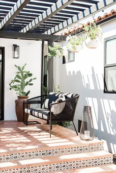 an outdoor patio with black and white furniture under a pergolated awning next to a potted plant