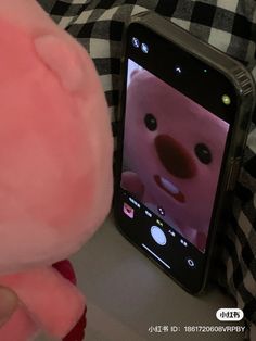 a pink teddy bear next to a cell phone with an animated face on the screen