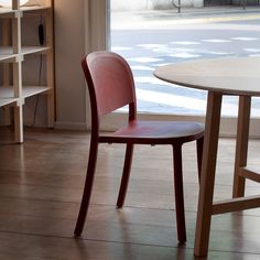 a red chair sitting in front of a window next to a table and book shelf